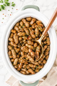 Southern crockpot boiled peanuts in a white slow cooker with a gold spoon scooping peanuts on a marble countertop with parsley and red pepper flakes