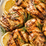 Juicy sweet tea brined grilled chicken thighs on a white platter with lemon slices and fresh rosemary