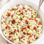 Creamy garlic BLT tortellini pasta salad in a white bowl topped with crispy bacon, diced tomatoes, chopped chives, and a rich garlic dressing on a marble countertop.