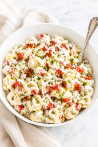 Creamy garlic BLT tortellini pasta salad in a white bowl topped with crispy bacon, diced tomatoes, chopped chives, and a rich garlic dressing on a marble countertop.