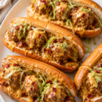 Toasted bacon cheeseburger meatball subs topped with creamy cheddar cheese sauce, crispy bacon, and shredded lettuce on a white platter.