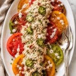 The best bacon jalapeño ranch chicken salad served over colorful heirloom tomato slices on a white platter with ranch drizzle, pickled jalapeños, and fresh chives.