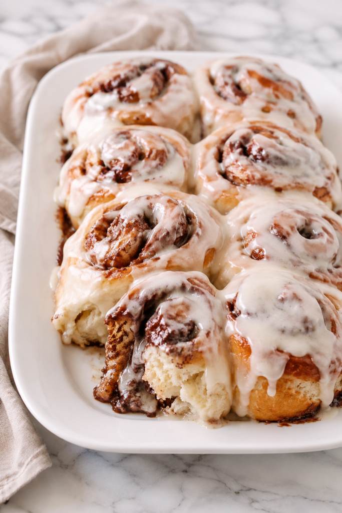 Soft and gooey Amish cinnamon rolls made with mashed potatoes and topped with creamy vanilla frosting on a white platter.
