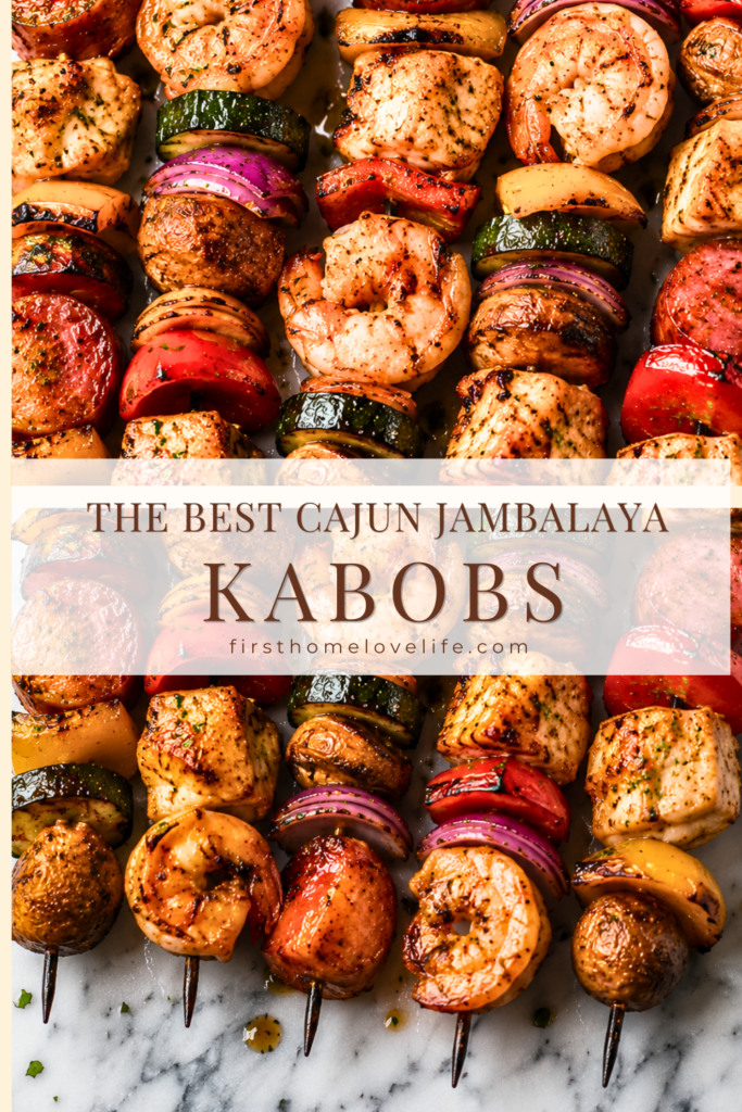 Grilled Cajun jambalaya kabobs loaded with chicken, shrimp, smoked sausage, bell peppers, red onion, zucchini, and mushrooms on a marble countertop.