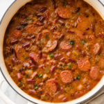 Southern red beans and rice with smoked sausage simmering in a white Dutch oven on a marble countertop.