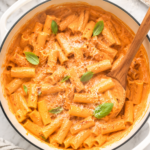 Creamy spicy rigatoni vodka pasta in a white enamel pot with Parmesan cheese and fresh basil on a marble countertop.