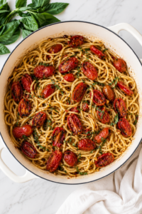 Brown butter tomatoes over spaghetti in a white Dutch oven topped with fresh basil on a white marble countertop.