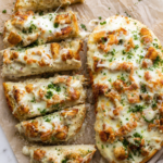 Creamy Cajun chicken Alfredo garlic bread topped with melted mozzarella and Parmesan on toasted French bread, served on wrinkled parchment over a white marble countertop.