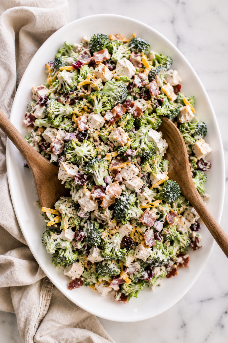Creamy chicken bacon ranch broccoli salad served on a white oval platter with wooden salad tossers on a marble countertop.