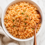 Copycat Texas Roadhouse seasoned rice served in a white bowl with a copper spoon on a white marble countertop and neutral linen towel.