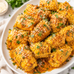 Copycat Wingstop fried corn on a white platter topped with Cajun butter sauce, fresh parsley, and grated Parmesan cheese on a marble countertop with a neutral linen cloth.