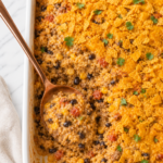 Creamy taco rice casserole with seasoned ground beef, black beans, corn, melted cheese, and crunchy crushed Doritos baked in a white casserole dish on a marble countertop.
