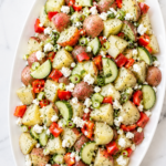 Fresh dill potato salad with feta cheese, red potatoes, cucumber, bell pepper, and scallions served on a white platter.
