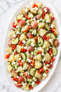 Fresh dill potato salad with feta cheese, red potatoes, cucumber, bell pepper, and scallions served on a white platter.