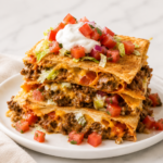 Easy Crunchwrap Supreme Casserole stacked on a white plate with seasoned ground beef, melted cheese, sour cream, and fresh pico de gallo on a marble countertop.