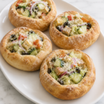 Rustic homemade bread bowls filled with Olive Garden-style salad featuring crisp lettuce, cucumbers, tomatoes, black olives, red onion, croutons, and grated Parmesan cheese served on a white platter over a marble countertop.
