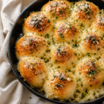 Extra garlic and cheesy bagna cauda rolls baked in a cast iron skillet with melted garlic butter, Parmesan cheese, and herbs on a white marble countertop.