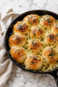 Extra garlic and cheesy bagna cauda rolls baked in a cast iron skillet with melted garlic butter, Parmesan cheese, and herbs on a white marble countertop.
