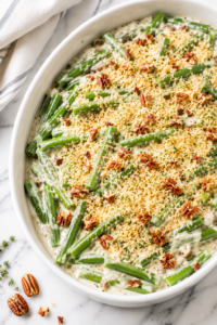 Creamy green bean goat cheese gratin topped with Parmesan breadcrumbs and chopped pecans in a white baking dish on a marble countertop.