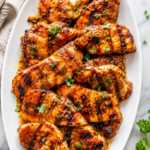Juicy grilled Catalina dressing chicken on a white serving platter with caramelized grill marks on a marble countertop.