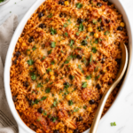 Chicken Tinga Rice Casserole baked with shredded chicken, Mexican rice, black beans, corn, melted cheese, and fresh cilantro in a white oval casserole dish.