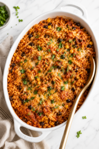 Chicken Tinga Rice Casserole baked with shredded chicken, Mexican rice, black beans, corn, melted cheese, and fresh cilantro in a white oval casserole dish.