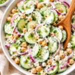 White bowl of high protein creamy cucumber salad with chickpeas, feta cheese, red onions, and fresh dill in a Greek yogurt dressing on a marble countertop.