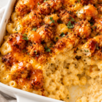 Creamy hot honey chicken mac and cheese in a white baking dish with crispy chicken pieces, drizzled with hot honey on a white marble countertop with a gold spoon and neutral kitchen towel.