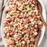 Creamy Italian grinder bean salad with cannellini beans, chickpeas, salami, pepperoni, provolone cheese, cherry tomatoes, olives, pepperoncini, and creamy Italian dressing served on a white platter.