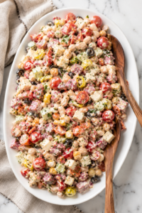 Creamy Italian grinder bean salad with cannellini beans, chickpeas, salami, pepperoni, provolone cheese, cherry tomatoes, olives, pepperoncini, and creamy Italian dressing served on a white platter.