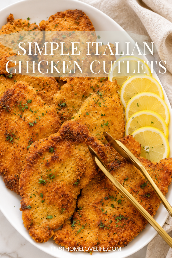 Golden crispy Italian chicken cutlets served on a white platter with fresh lemon slices and gold serving tongs on a marble countertop.