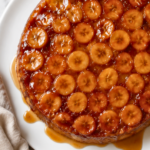 Banana Foster upside down cake on a white plate with caramelized banana slices, buttery caramel dripping onto the plate