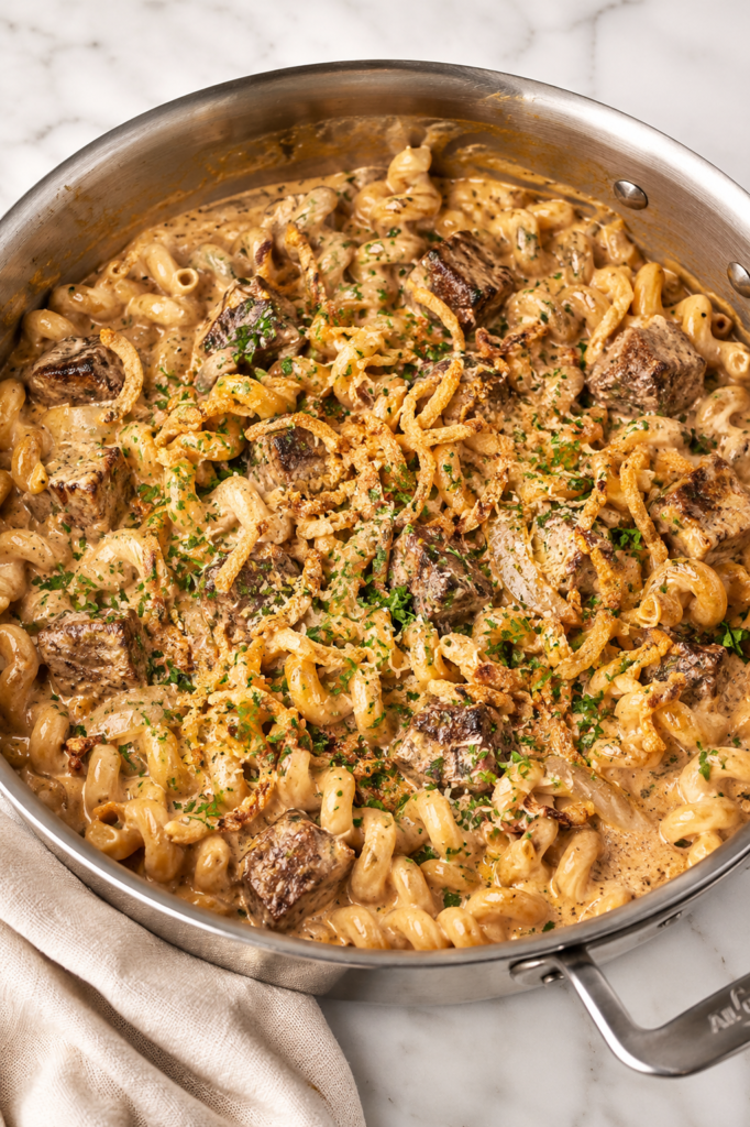 Creamy Bloomin' Onion steak bite pasta made in one pan with tender seared steak bites, cavatappi pasta, caramelized onions, crispy fried onions, and a rich, cheesy cream sauce.