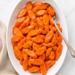Orange juice glazed carrots with parsley on a white serving platter