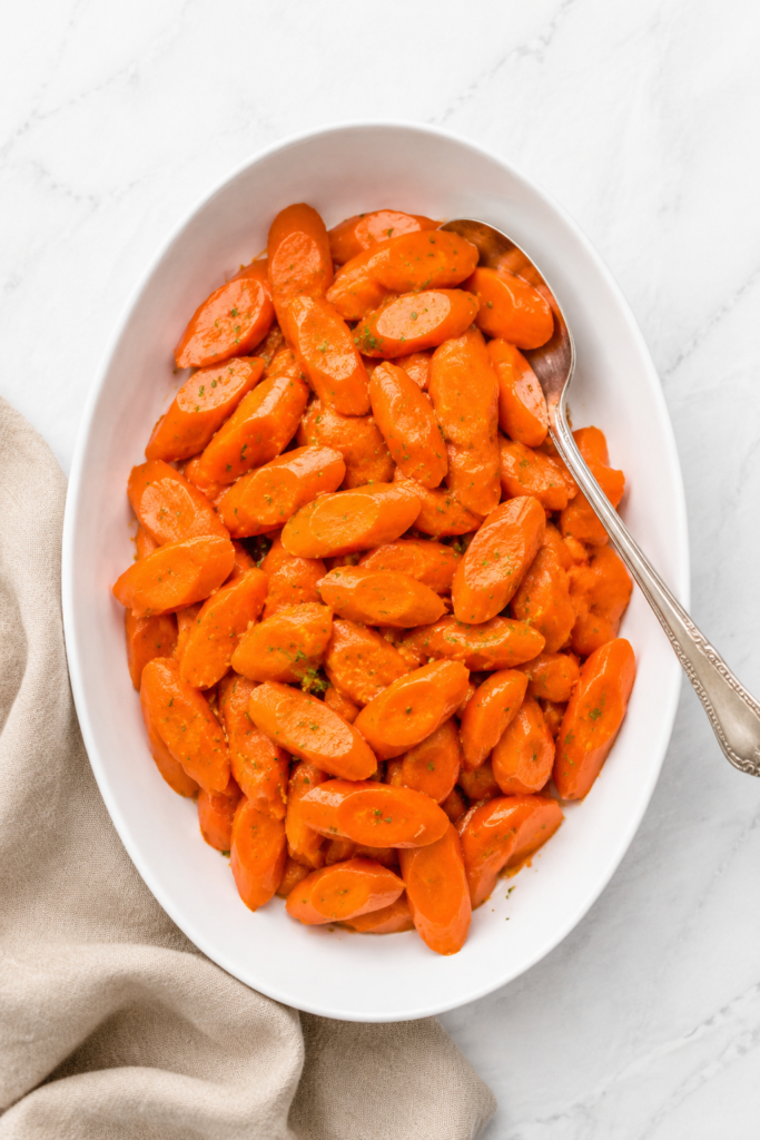 Orange juice glazed carrots with parsley on a white serving platter