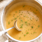 Homemade turkey gravy from scratch with pan drippings, parsley, and cracked black pepper in a stainless steel saucepan with a silver ladle.