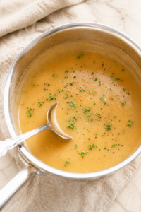 Homemade turkey gravy from scratch with pan drippings, parsley, and cracked black pepper in a stainless steel saucepan with a silver ladle.
