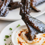 Whole black chicken wing being dipped into creamy ranch dressing swirled with spicy chili crisp.