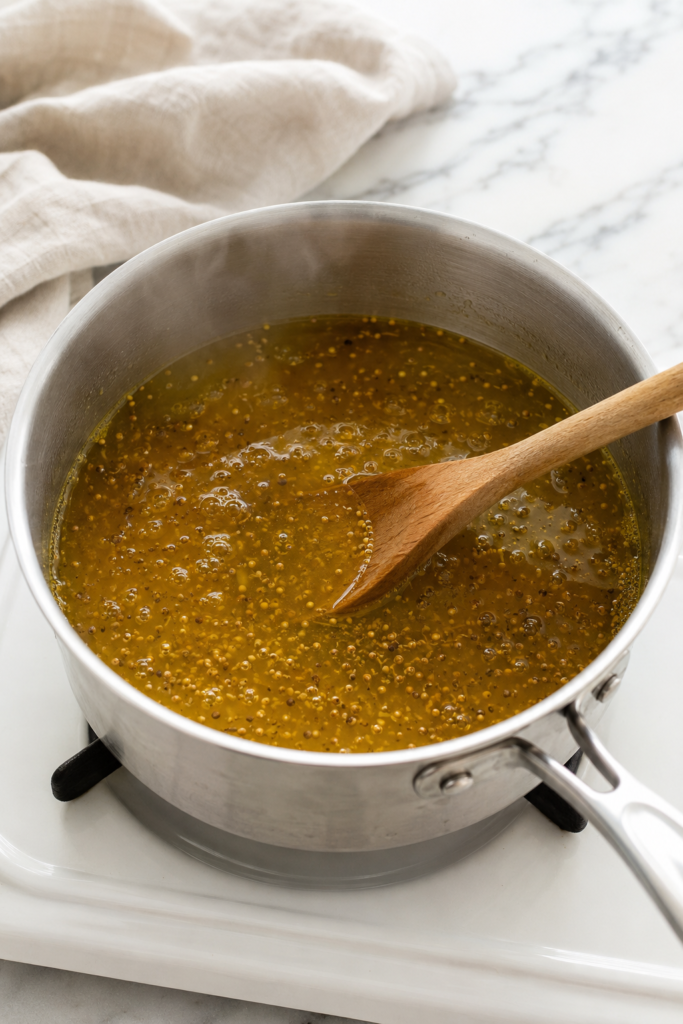 Golden bread and butter pickle brine simmering with mustard seeds, celery seeds, and turmeric in a stainless-steel saucepan.