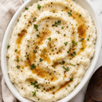 Creamy brown butter mashed potatoes in a white serving bowl topped with golden brown butter, fresh herbs, and cracked black pepper.