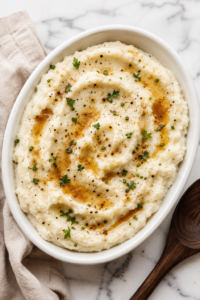 Creamy brown butter mashed potatoes in a white serving bowl topped with golden brown butter, fresh herbs, and cracked black pepper.