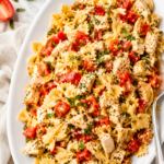 Bruschetta chicken pasta served on a white platter with grilled chicken, fresh tomatoes, basil, Parmesan cheese, and balsamic glaze.