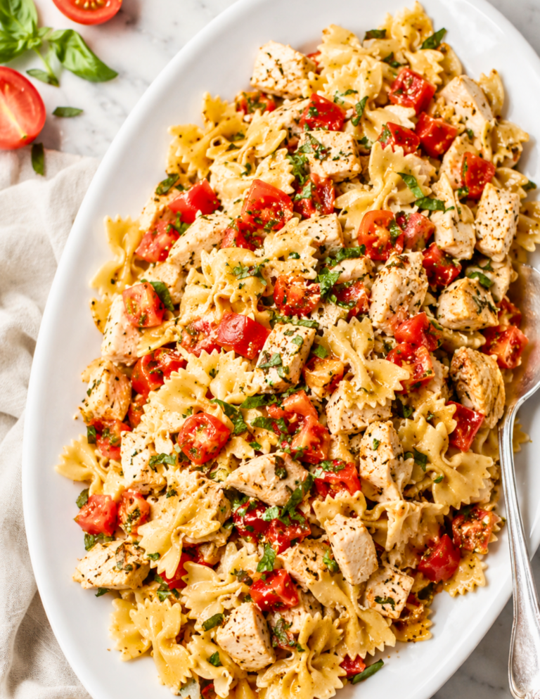 Bruschetta chicken pasta served on a white platter with grilled chicken, fresh tomatoes, basil, Parmesan cheese, and balsamic glaze.