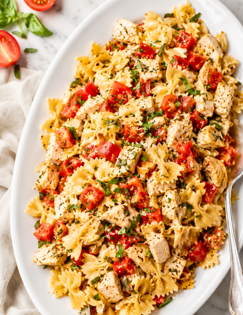 Bruschetta chicken pasta served on a white platter with grilled chicken, fresh tomatoes, basil, Parmesan cheese, and balsamic glaze.
