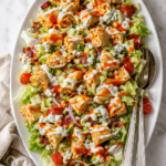 Buffalo chicken taquito chopped salad with iceberg lettuce, bacon, tomatoes, blue cheese, ranch dressing, and buffalo sauce