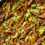 Chinese beef and cabbage stir fry with sliced steak, cabbage, carrots, onions, and savory garlic ginger sauce in a cast-iron skillet.