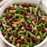 Classic green bean and bean salad with kidney beans, chickpeas, green beans, and red onion in a white serving bowl with a tangy homemade dressing.