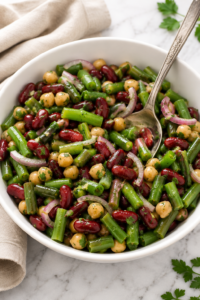 Classic green bean and bean salad with kidney beans, chickpeas, green beans, and red onion in a white serving bowl with a tangy homemade dressing.
