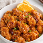 Copycat Panda Express Hot Orange Chicken coated in a sticky spicy orange sauce with red chilies, sesame seeds, green onions, and fresh orange slices.