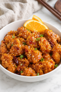Copycat Panda Express Hot Orange Chicken coated in a sticky spicy orange sauce with red chilies, sesame seeds, green onions, and fresh orange slices.